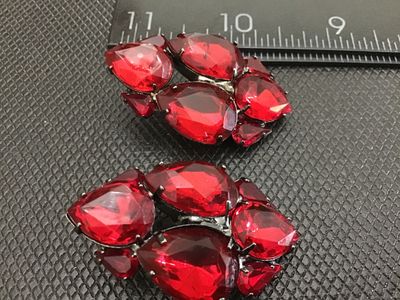 Sale Photo Thumbnail #4: Pair of vintage cluster clip-on earrings featuring multi-faceted, teardrop-cut red rhinestones set in gunmetal tone metal backings. Each earring measures approximately 1.5 inches in length. In good condition with functional clip closures and light surface