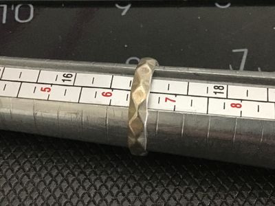 Sale Photo Thumbnail #219: A silver-tone metal ring featuring a geometric, faceted/hammered exterior texture. Ring size measures approximately 6.75 on a ring sizer mandrel. Item shows slight surface wear consistent with age and use.