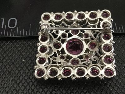 Sale Photo Thumbnail #177: A square-shaped vintage costume brooch featuring a central large round pink rhinestone surrounded by smaller, vibrant pink rhinestones set in silver-tone ornate filigree metalwork. Features a standard pin back with a safety clasp. Measures approximately 1