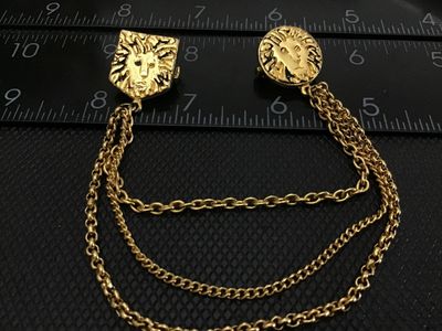 Sale Photo Thumbnail #89: A vintage Anne Klein gold-tone double brooch featuring textured lion head motifs connected by a multi-strand dangled chain. Marked ANNE KLEIN on the back of the shield-shaped pin. Features rollover safety clasp closures. In good vintage condition with lig