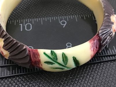 Sale Photo Thumbnail #60: Vintage carved Celluloid bangle bracelet featuring painted floral and fan details in red, green, brown, and cream tones. Measures approximately 3 inches in outer diameter. Shows minor surface wear consistent with age.