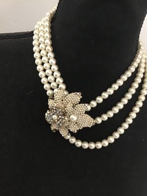Sale Photo Thumbnail #104: A vintage triple-strand faux pearl necklace featuring an elaborate side clasp decorated with beaded seed pearls and aurora borealis rhinestones in a floral motif. Marked "JAPAN" on the back of the metal setting. Shows light age-appropriate wear, including