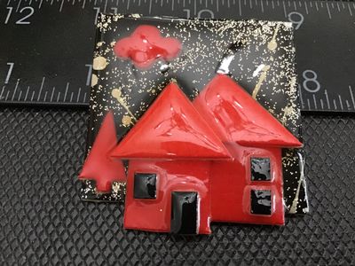 Sale Photo Thumbnail #71: A vintage artisan brooch labeled 'House Pins by Lucinda', Portland, ME. Features a colorful red house scene against a black background with gold glitter accents. Crafted with resin/plastic materials and a rollover safety clasp on the reverse. Measures app