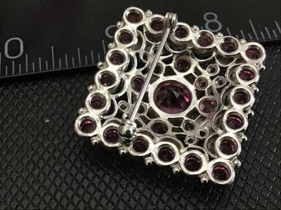 Sale Photo Thumbnail #176: A square-shaped vintage costume brooch featuring a central large round pink rhinestone surrounded by smaller, vibrant pink rhinestones set in silver-tone ornate filigree metalwork. Features a standard pin back with a safety clasp. Measures approximately 1