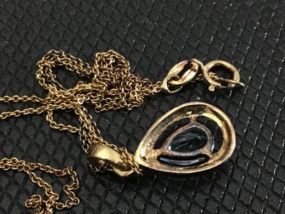 Sale Photo Thumbnail #180: Gold-tone fine link chain necklace featuring a teardrop/pear-cut light blue stone pendant surrounded by a textured silver-tone halo bezel. The pendant shows light wear on the back metal setting. Includes a spring ring clasp. Pendant measures approximately