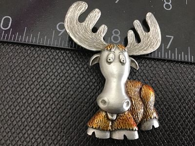 Sale Photo Thumbnail #150: A whimsical vintage pewter moose brooch by JJ (Jonette Jewelry). Features detailed textured fur, large antlers, and a fun expressions with brown painted accents. Stamped "©JJ" on the reverse. Measures approximately 2 inches tall. In good vintage conditio