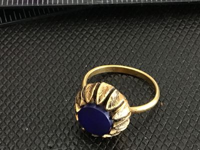 Sale Photo Thumbnail #192: Vintage gold tone cocktail ring featuring a textured crown/petal bezel and a round, flat dark blue cabochon insert. The band appears adjustable. Ring size measures approximately size 7 to 7.5 on a ring mandrel. Good vintage condition with light wear consi