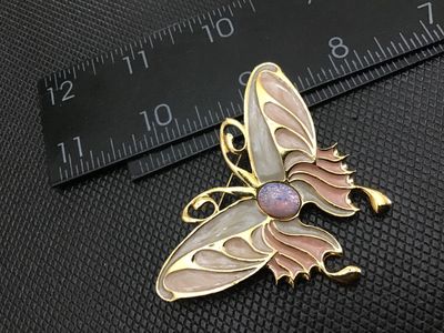 Sale Photo Thumbnail #36: Gold-tone butterfly brooch featuring multi-color pearlescent enamel wings in shades of pink and grey, accented with a purple/iridescent faux opal cabochon center. Pin back clasp is intact and functions properly. Measures approximately 2.5 inches wide. Goo