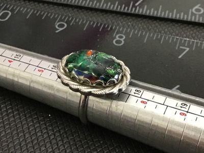 Sale Photo Thumbnail #142: Vintage statement ring featuring an oval green, black, and multicolor art glass cabochon set in a scalloped, rope-twist silver tone bezel. The ring has an adjustable band as shown in the photos. Measures approximately size 8 to 9 as shown on the ring size