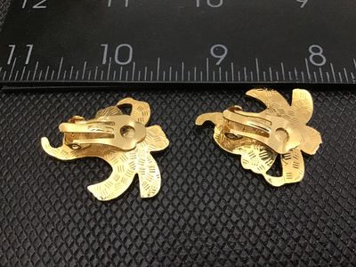 Sale Photo Thumbnail #6: Pair of floral clip-on earrings featuring a lily design in deep blue and purple enamel with gold-tone accents and textured gold-tone backs. Each earring measures approximately 1.25 inches in length. In good pre-owned vintage condition with functional clip