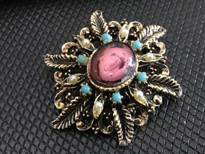 Sale Photo Thumbnail #209: Vintage gold-tone ornate filigree brooch featuring a central oval pink cabochon accented by faux pearls and turquoise-color beads. Features a safety pin clasp closure on the back. Shows light surface wear and finish aged patina consistent with age. Measur