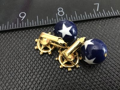 Sale Photo Thumbnail #140: Pair of gold-tone clip-on earrings featuring a nautical ship's wheel with red enamel star accents, dangling blue beads decorated with white stars. Patriotic red, white, and blue motif. Good vintage condition with light wear on metal finish.