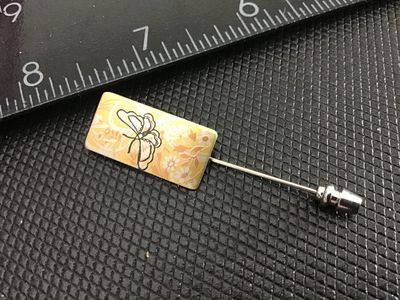 Sale Photo Thumbnail #197: A vintage Reed & Barton Damascene rectangular stick pin featuring a butterfly and floral motif in gold, silver, and black tones on a yellow background. Marked 'Reed & Barton Damascene' on the reverse. Measures approximately 2 inches in total length includ