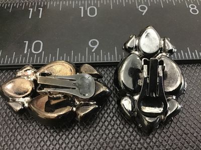 Sale Photo Thumbnail #2: Pair of vintage cluster clip-on earrings featuring multi-faceted, teardrop-cut red rhinestones set in gunmetal tone metal backings. Each earring measures approximately 1.5 inches in length. In good condition with functional clip closures and light surface