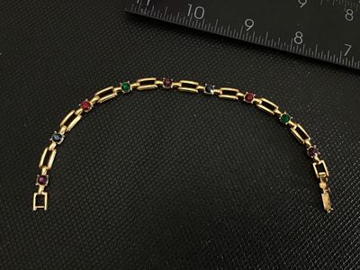 Sale Photo Thumbnail #214: A vintage gold-tone open bar-link bracelet featuring round, bezel-set multi-colored rhinestones in red, green, blue, and purple. Measures approximately 7 inches in length and features a fold-over clasp closure. Shows light signs of wear consistent with ag