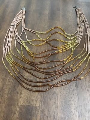 Sale Photo Thumbnail #125: Multi-strand statement necklace featuring earth-toned amber and honey-colored glass bugle beads layered with natural light brown heishe/stone beads. Finished with textured metal end cones and an adjustable hook-and-chain closure. Appears to be in very goo