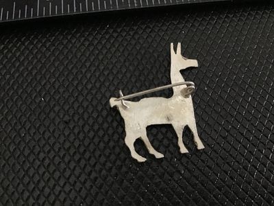 Sale Photo Thumbnail #218: A silver-tone metal pin crafted in the shape of a llama or alpaca featuring textured fur detailing and a saddle back. Pin back fastener on the reverse. Measures approximately 1.25 inches long. Shows light patina and wear consistent with age.