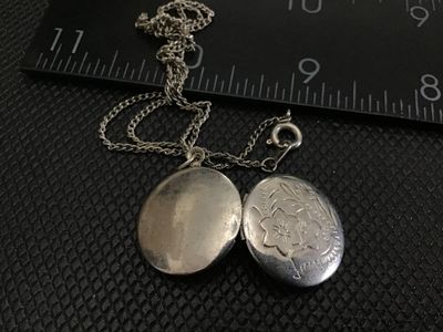 Sale Photo Thumbnail #49: A vintage oval locket pendant necklace featuring an etched floral motif on the front cover. The locket opens to reveal space for two small photos. Comes attached to a fine chain with a spring ring clasp. Shows light tarnishing and wear consistent with age