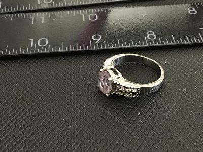 Sale Photo Thumbnail #167: Stainless steel ring featuring a central light purple oval-cut stone flanked by clear accent stones down the shoulders. Marked '316L SS' on the interior band. Ring measures approximately size 9 on the mandrel. Good condition with light surface wear.