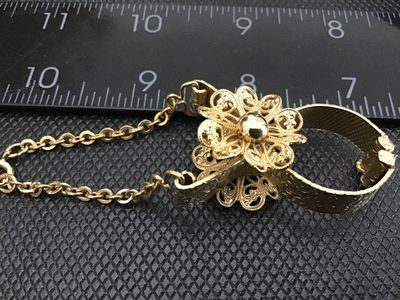 Sale Photo Thumbnail #46: Vintage gold-tone metal glove clip featuring a delicate filigree flower center design, textured metal band clip, and an attached safety chain with spring ring clasp. Decorative antique/vintage fashion accessory. Measures approximately 3 to 4 inches in len