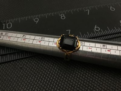 Sale Photo Thumbnail #15: Gold-tone fashion ring featuring a large, emerald-cut black onyx-style stone set in a openwork framework setting with decorative split shoulders. Shown on a ring mandrel measuring approximately size 7.5. Shows minor surface wear and finish rubbing consist