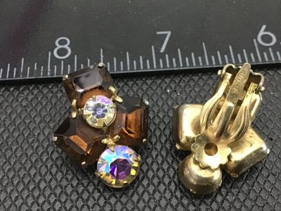Sale Photo Thumbnail #129: Pair of vintage clip-on earrings featuring emerald-cut amber glass stones paired with sparkling round aurora borealis rhinestones in a gold-tone prong setting. Marked PAT. PEND. on the clip backs. Each earring measures approximately 1 inch in size. Good v