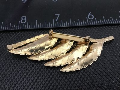 Sale Photo Thumbnail #147: A vintage gold-tone brooch featuring a cascading layered leaf motif with textured detail, accenting a curved line of clear set rhinestones along the top edge. The piece measures approximately 2.5 inches in length. Features a classic pin-back closure with 