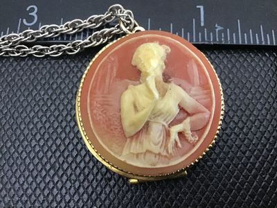 Sale Photo Thumbnail #42: Vintage costume jewelry necklace featuring a round hinged locket with a faux cameo motif depicting a classic female profile against a peachy-pink background set in a gold-tone beaded bezel. Attached to a silver-tone/gold-tone chain. The pendant measures a