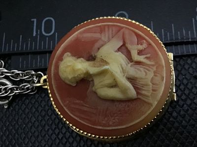 Sale Photo Thumbnail #41: Vintage costume jewelry necklace featuring a round hinged locket with a faux cameo motif depicting a classic female profile against a peachy-pink background set in a gold-tone beaded bezel. Attached to a silver-tone/gold-tone chain. The pendant measures a