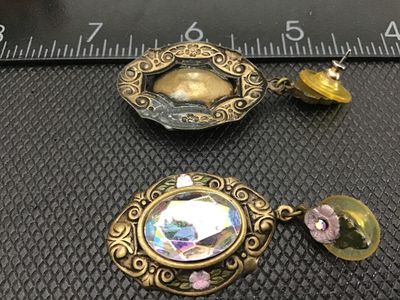 Sale Photo Thumbnail #83: Pair of vintage-style drop/dangle pierce-back earrings featuring an ornate brass-tone filigree metal frame, small floral accent detail with pink enamel, and large multifaceted iridescent aurora borealis rhinestones/glass stones. Measures approximately 2 i