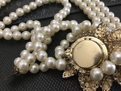 Sale Photo Thumbnail #101: A vintage triple-strand faux pearl necklace featuring an elaborate side clasp decorated with beaded seed pearls and aurora borealis rhinestones in a floral motif. Marked "JAPAN" on the back of the metal setting. Shows light age-appropriate wear, including