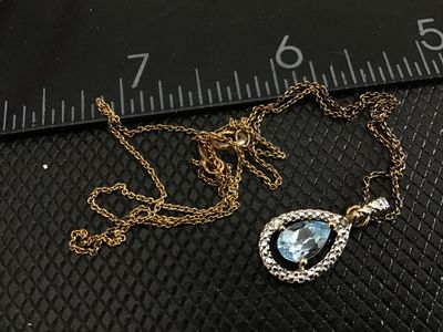 Sale Photo Thumbnail #181: Gold-tone fine link chain necklace featuring a teardrop/pear-cut light blue stone pendant surrounded by a textured silver-tone halo bezel. The pendant shows light wear on the back metal setting. Includes a spring ring clasp. Pendant measures approximately