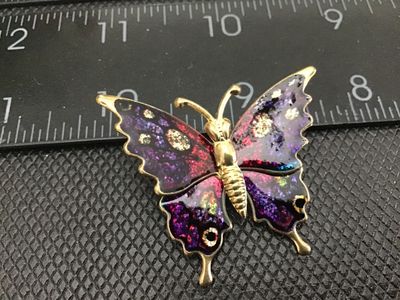Sale Photo Thumbnail #69: Gold-tone butterfly brooch featuring vibrant purple, pink, and iridescent glitter enamel details. Measures approximately 2 inches in width. Standard pin back mechanism. Shows minor vintage wear on the back side, otherwise in good pre-owned condition.