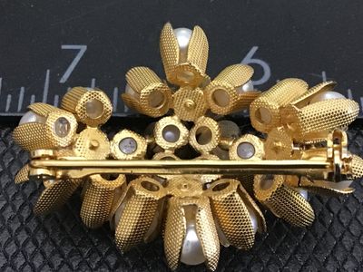 Sale Photo Thumbnail #92: A vintage gold-tone floral cluster brooch featuring faux pearls encased in textured, petal-like cups along with clear rhinestone accents. The pin measures approximately 1.5 inches in length. Features a standard pin back with a safety clasp mechanism. Exce