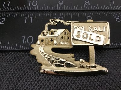 Sale Photo Thumbnail #67: Vintage gold-tone costume jewelry brooch depicting a house with a chimney and a real estate sign reading "FOR SALE" with a "SOLD" overlay. Features a pin back closure with a safety clasp. Shows light vintage wear and finish loss around the edges. Measures