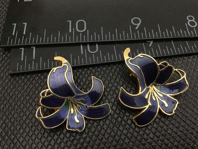 Sale Photo Thumbnail #5: Pair of floral clip-on earrings featuring a lily design in deep blue and purple enamel with gold-tone accents and textured gold-tone backs. Each earring measures approximately 1.25 inches in length. In good pre-owned vintage condition with functional clip