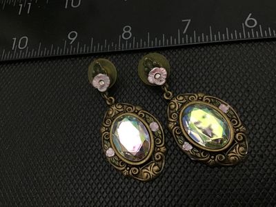 Sale Photo Thumbnail #82: Pair of vintage-style drop/dangle pierce-back earrings featuring an ornate brass-tone filigree metal frame, small floral accent detail with pink enamel, and large multifaceted iridescent aurora borealis rhinestones/glass stones. Measures approximately 2 i
