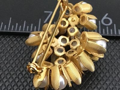 Sale Photo Thumbnail #93: A vintage gold-tone floral cluster brooch featuring faux pearls encased in textured, petal-like cups along with clear rhinestone accents. The pin measures approximately 1.5 inches in length. Features a standard pin back with a safety clasp mechanism. Exce