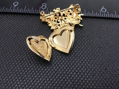 Sale Photo Thumbnail #134: Vintage gold-tone brooch pin featuring a cherub/angel motif with the words 'SOMEONE SPECIAL' in detailed scrollwork, holding a dangling opening heart locket with an engraved double-heart design. Measures approximately 2 inches wide. Pin clasp mechanism wo