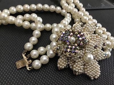 Sale Photo Thumbnail #100: A vintage triple-strand faux pearl necklace featuring an elaborate side clasp decorated with beaded seed pearls and aurora borealis rhinestones in a floral motif. Marked "JAPAN" on the back of the metal setting. Shows light age-appropriate wear, including