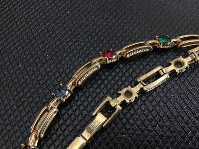 Sale Photo Thumbnail #216: A vintage gold-tone open bar-link bracelet featuring round, bezel-set multi-colored rhinestones in red, green, blue, and purple. Measures approximately 7 inches in length and features a fold-over clasp closure. Shows light signs of wear consistent with ag
