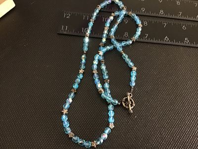 Sale Photo Thumbnail #233: A beaded necklace featuring light blue iridescent/aurora borealis faceted crystal beads, interspersed with silver-tone floral spacer beads and finished with a toggle clasp closure. Measures approximately 22 to 24 inches in total length. Overall good pre-o