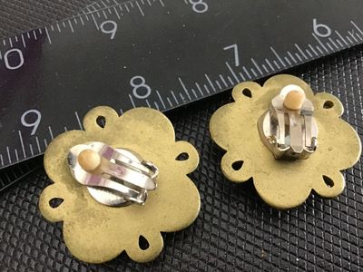Sale Photo Thumbnail #208: Pair of vintage gold-tone clip-on earrings featuring vibrant, multi-colored glass or resin oval cabochons in red, green, blue, and purple. Designed in a flower or starburst pattern with textured rope-style borders. Measure approximately 1 inch in diameter