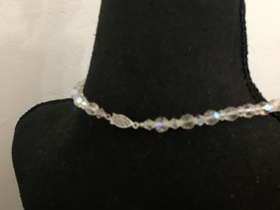 Sale Photo Thumbnail #119: A vintage single-strand necklace featuring faceted clear glass beads with an iridescent Aurora Borealis (AB) coating. The necklace is finished with a filigree push-in box clasp. Appears to be in good vintage condition with no missing beads observed.