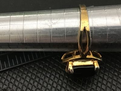 Sale Photo Thumbnail #16: Gold-tone fashion ring featuring a large, emerald-cut black onyx-style stone set in a openwork framework setting with decorative split shoulders. Shown on a ring mandrel measuring approximately size 7.5. Shows minor surface wear and finish rubbing consist