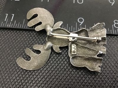 Sale Photo Thumbnail #151: A whimsical vintage pewter moose brooch by JJ (Jonette Jewelry). Features detailed textured fur, large antlers, and a fun expressions with brown painted accents. Stamped "©JJ" on the reverse. Measures approximately 2 inches tall. In good vintage conditio