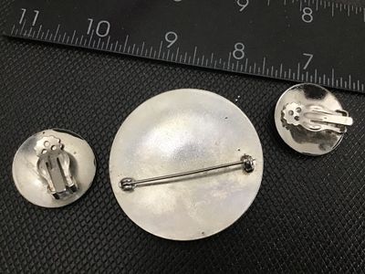 Sale Photo Thumbnail #153: A 3-piece vintage costume jewelry set featuring a circular silver-tone brooch pin and matching clip-on earrings. Each piece features applied raised details of a textured owl and a man-in-the-moon crescent face. The brooch measures approximately 2 inches i