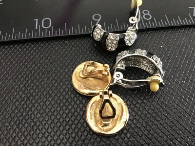 Sale Photo Thumbnail #163: Lot of 2 pairs of vintage clip-on earrings. Includes one pair of silver-tone hoop-style clip earrings with black enamel and clear rhinestone accents, and one pair of gold-tone oval clip earrings featuring black cabochons or enamel centers surrounded by cl
