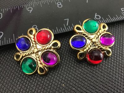 Sale Photo Thumbnail #207: Pair of vintage gold-tone clip-on earrings featuring vibrant, multi-colored glass or resin oval cabochons in red, green, blue, and purple. Designed in a flower or starburst pattern with textured rope-style borders. Measure approximately 1 inch in diameter