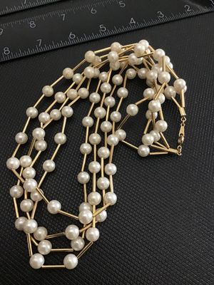 Sale Photo Thumbnail #108: A multi-strand vintage costume necklace featuring cream-colored faux pearls interspersed with gold-tone rigid bar links, creating a dramatic structured lattice or cage effect. Secured with a spring-ring clasp. Shown on a jewelry display bust and alongside